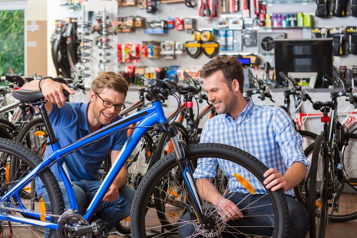 Man buying a bicycle in bike store, talking with shop assistant and watching the mountain bike together.